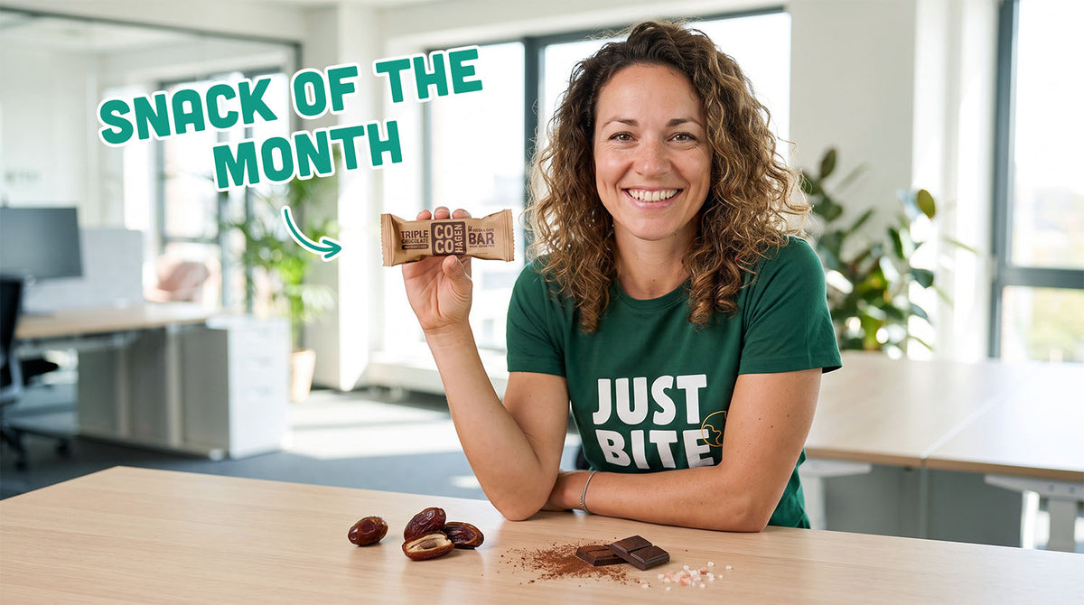 Cocohagen Triple Chocolate biologische dadel-cacaoreep, uitgelicht als 'Snack of the Month' door een JustBite medewerker, omringd door ingrediënten zoals smeuïge dadels, cacaopoeder, pure chocolade en roze zeezout.