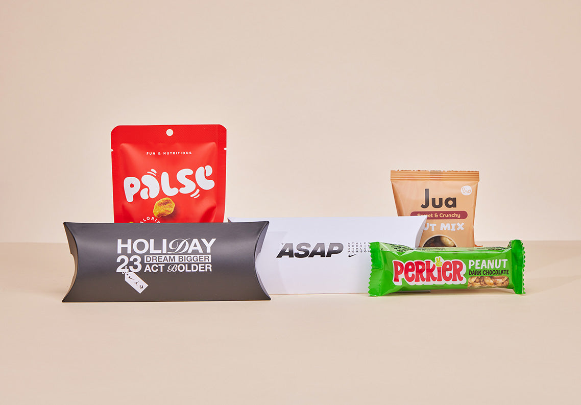 Gepersonaliseerde JustBite pillowbox met het Nike ASAP-logo, omringd door diverse bewuste snacks zoals Perkier en Jua.