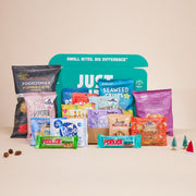Een geopend JustBite Eindejaarsgeschenk Large gevuld met een ruim assortiment aan bewuste snacks, omringd door subtiele kerstdecoratie zoals mini-boompjes en dennenappels.