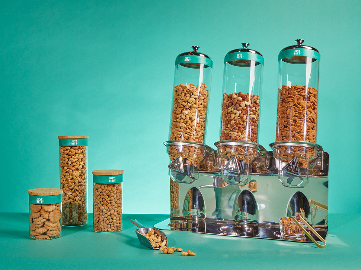 Glazen snackdispensers en voorraadpotten gevuld met diverse bulknoten en hartige snacks tegen een turquoise achtergrond.