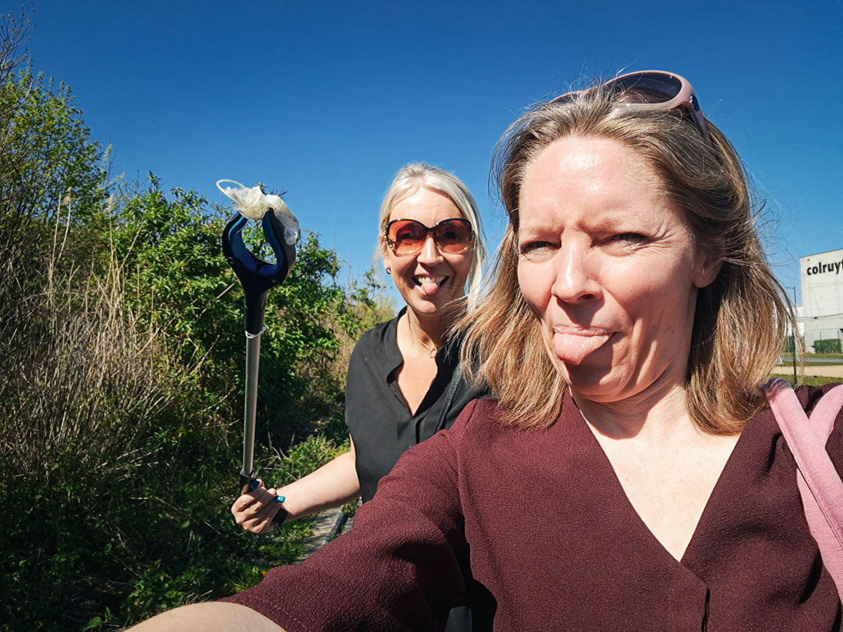 JustBite collega's Lynn en Charlotte nemen een selfie tijdens het ploggen op een zonnige dag, met een grijper en opgeraapt zwerfvuil in de hand.