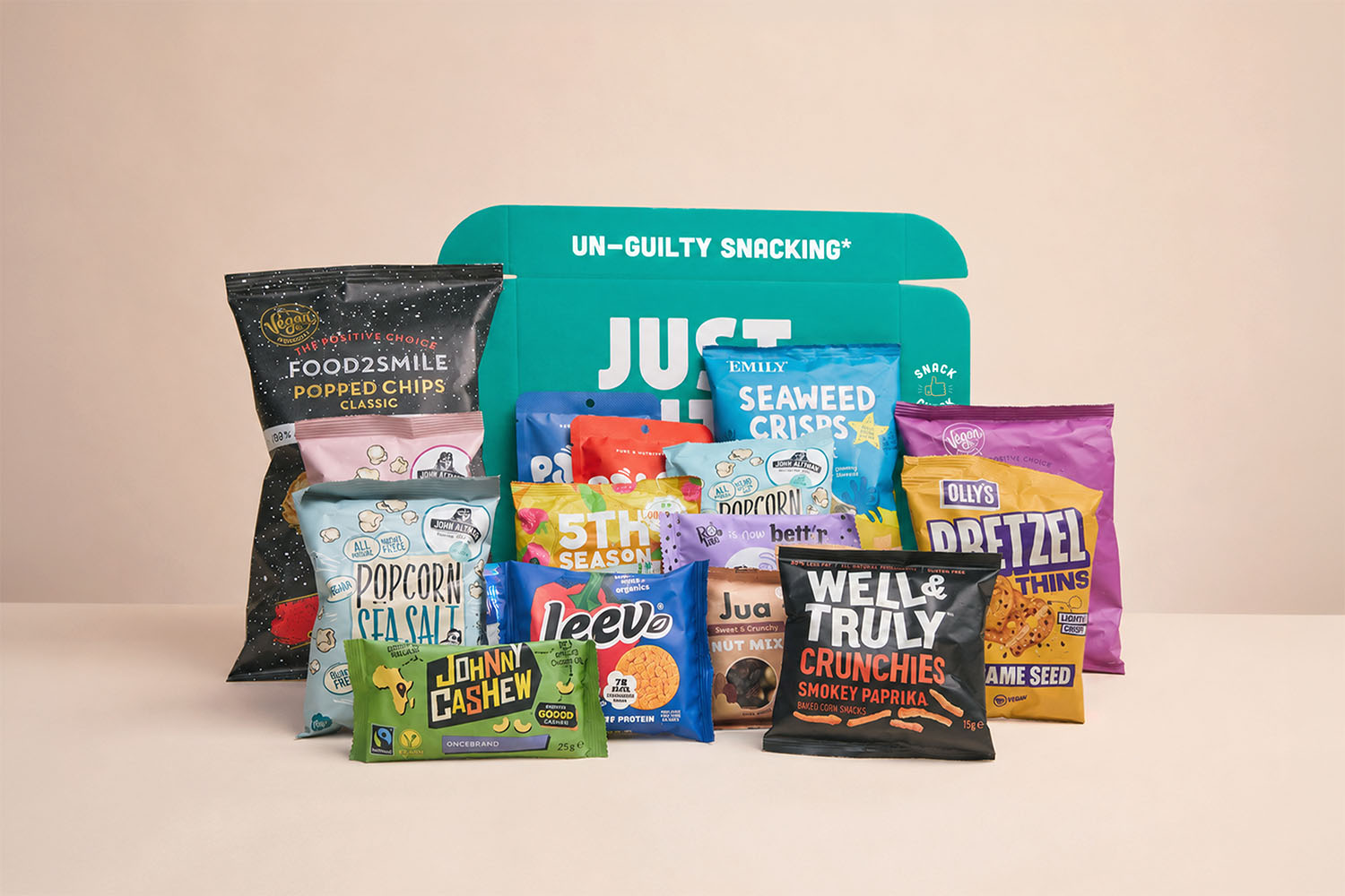 Een geopend JustBite eindejaarsgeschenk met een ruim assortiment aan hartige en knapperige snacks, waaronder pops, chips en noten tegen een zachte achtergrond.