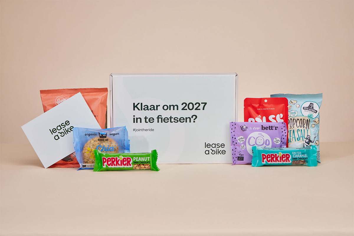 Een gepersonaliseerde JustBite geschenkbox voor Lease a Bike met de opdruk 'Klaar om 2027 in te fietsen?', gevuld en omringd met diverse bewuste snacks en een gegraveerd kaartje.
