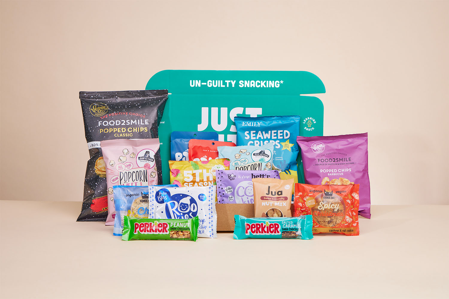 Een geopend JustBite eindejaarsgeschenk gevuld met een divers assortiment aan bewuste snacks, zowel hartig als zoet, waaronder popped chips, chocolade, koekjes en noten tegen een zachte achtergrond.