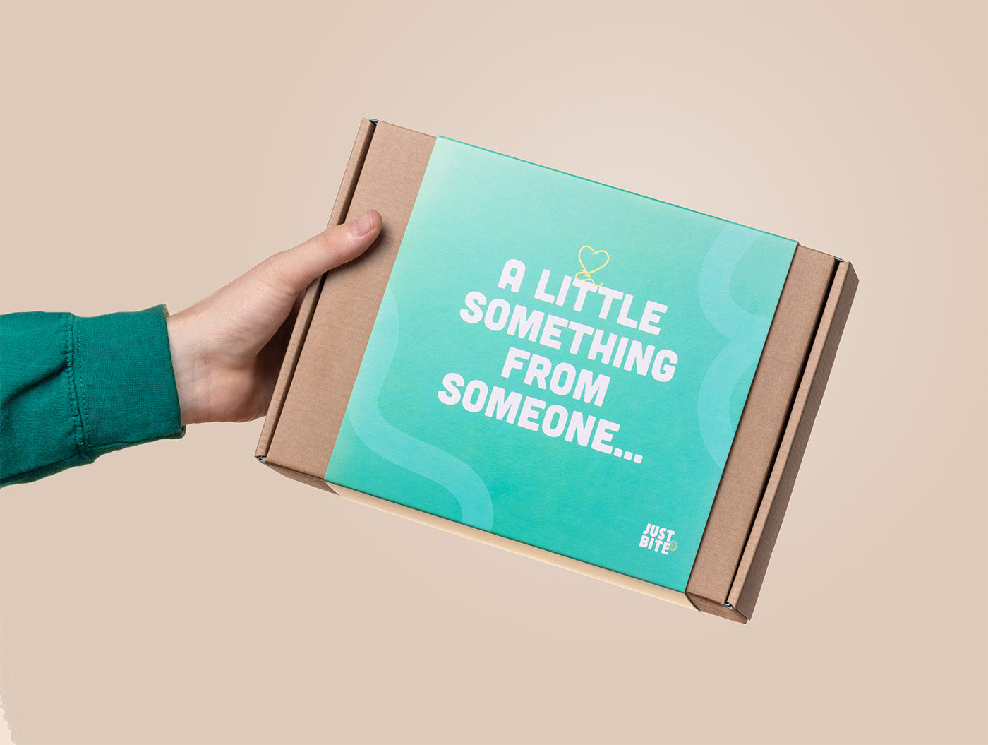 Een hand houdt een gecureerde JustBite gifting box vast met de opdruk 'A little something from someone...'. Dit attente relatiegeschenk maakt beter snacken makkelijk en is het perfecte gebaar om medewerkers of partners te verrassen met snacks die goed smaken én goed voelen.
