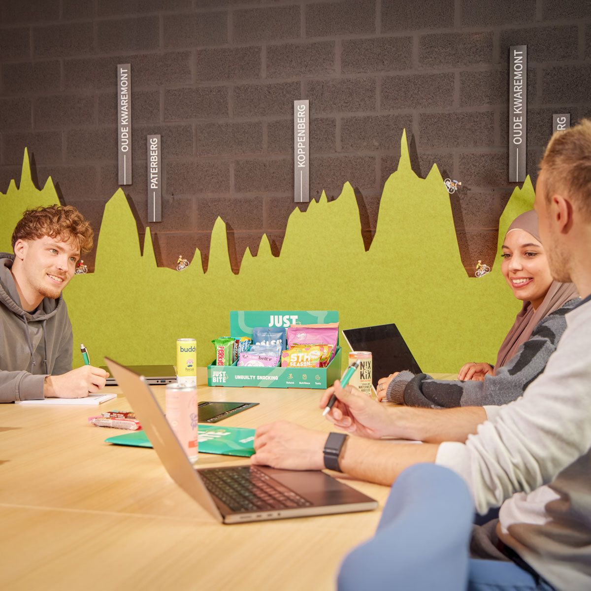 Een divers team lacht en praat tijdens een ontspannen moment met een JustBite snackbox op tafel. Een voorbeeld van hoe lekker eten verbindt en fungeert als brandstof voor een positieve bedrijfscultuur.