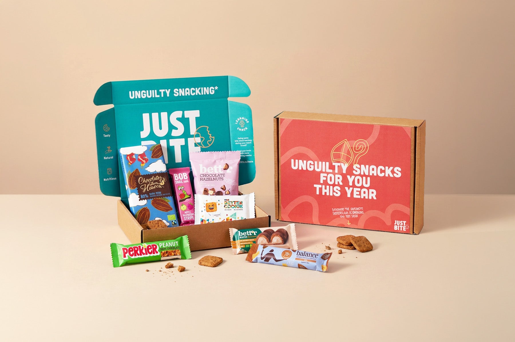 Een feestelijk JustBite sinterklaaspakket voor personeel. De open doos toont een selectie verrassend lekkere snacks zoals donkere chocolade, naast een rode theamdoos met de tekst 'Unguilty snacks for you this year'. Wij maken beter snacken makkelijk met bewuste geschenken waar je team onbezorgd van geniet.