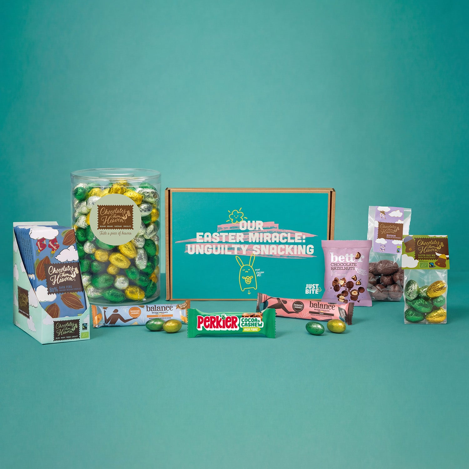 Een JustBite Paasgeschenkbox met de tekst 'Our Easter Miracle', omringd door diverse bewuste snacks en een bulk pot gevuld met kleurrijke chocolade-paaseitjes tegen een turquoise achtergrond.